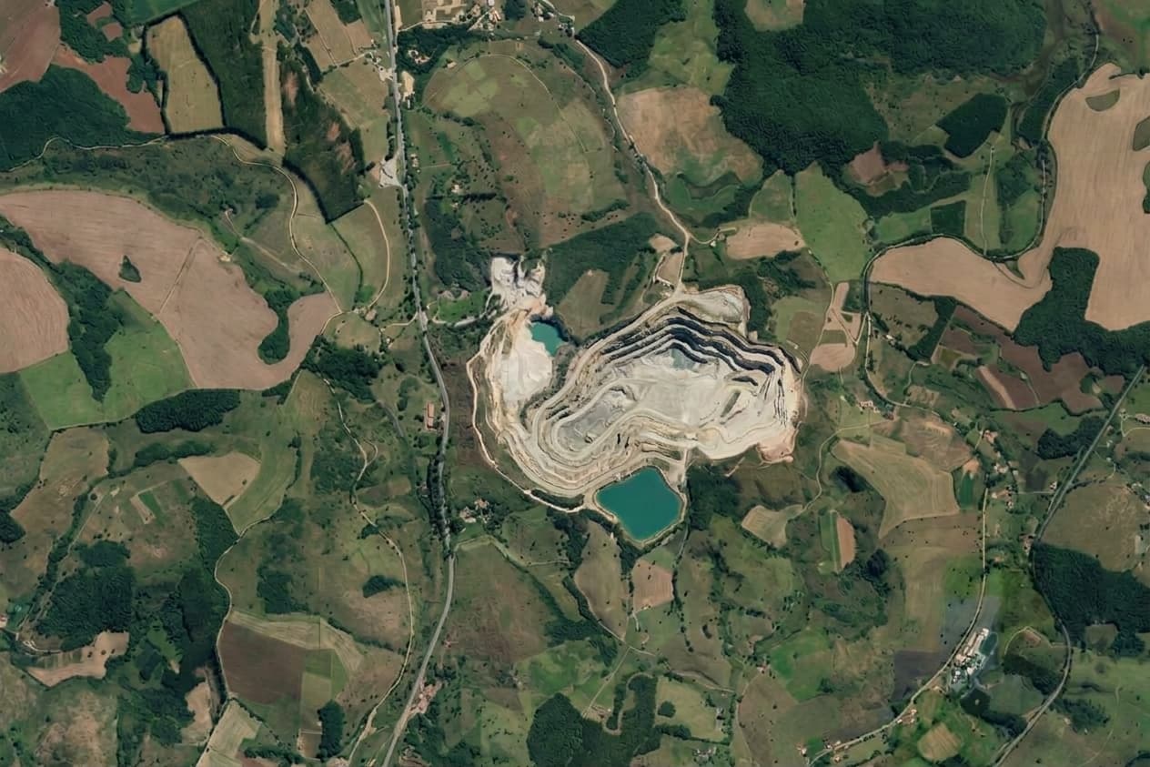 Vista de cima de uma mina a céu aberto com dois lagos, cercada por campos e vegetação.